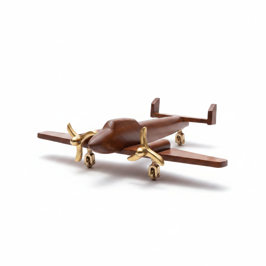 A small wooden airplane model with polished gold-colored metal propellers and landing gear, displayed on a light gray surface with a gray background.
