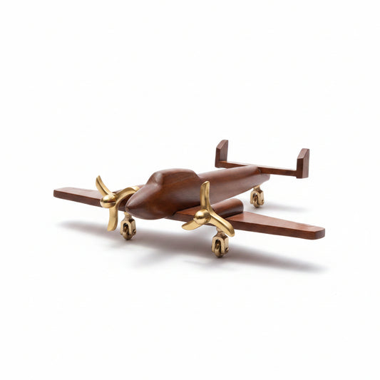A small wooden airplane model with polished gold-colored metal propellers and landing gear, displayed on a light gray surface with a gray background.